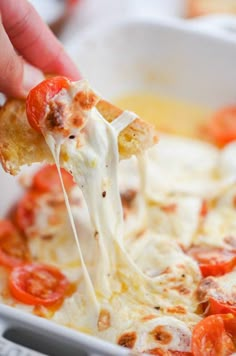 a person dipping cheese into a casserole dish with tomatoes on the side and bread croutons