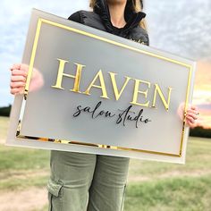 a woman holding up a sign that says haven salon studio in gold lettering on it