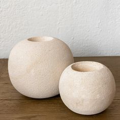 two white ceramic vases sitting on top of a wooden table next to each other