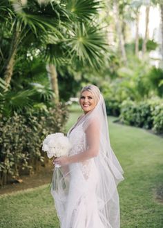 a woman in a wedding dress is holding a bouquet and posing for the camera with palm trees behind her