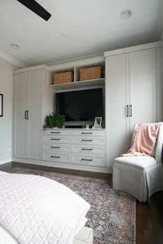 a bedroom with white furniture and a large flat screen tv mounted on the wall above it