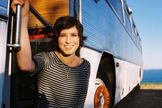 a woman standing in front of a bus with her hand on the door and smiling