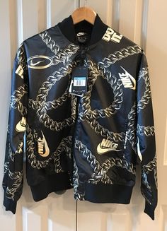 Elevate your activewear game with this gorgeous Nike Sportswear bomber jacket for women. The black and gold chain pattern adds a touch of glamour to any athleisure outfit. This loose-fit jacket is made of high-quality polyester and features a full zip closure and pockets to keep your essentials close at hand. The synthetic fill provides warmth and comfort during walks or cool outdoor activities. Machine washable for easy care, this Nike jacket is perfect for the woman who wants to stay comfortab Nike Icon Clash Jacket, Nike Varsity Jacket, Black Track Jacket With Graphic Print, Luxury Black Nike Track Jacket, Nike Black Sports Outerwear, Nike Tech Jacket, Black Moisture-wicking Track Jacket For Streetwear, Black Moisture-wicking Track Jacket For Sports, Nike Air Women