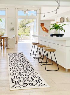 a white kitchen with an area rug on the floor and bar stools next to it