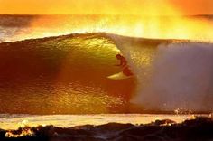 a man riding a wave on top of a surfboard in the ocean at sunset