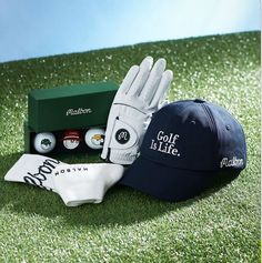 two hats, gloves and golf balls are on the grass near a green box that says'golf is life '