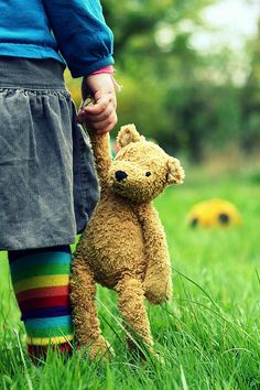 a child holding a teddy bear on top of a grass covered field with the words in spanish above it