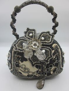 This beautiful Mary Frances handbag features a black and white floral pattern on a canvas exterior, with silver hardware accents and beaded trim. The bag has a magnetic closure and a top handle strap made of metal, while the lining material is fabric and the lining color is multicolor. The bag measures 6 inches in width, 5 inches in height, and 4 inches in depth.This handbag is a great addition to any woman's collection, with its unique style and customized beads and crystals. This Mary Frances bag is a high-quality item that is sure to impress. Mary Frances Bags, Mary Frances Handbags, Black And White Floral Pattern, Embellished Bags, Mary Frances, Timeless Chic, Purse Brands, Popular Fashion, Black And White Floral