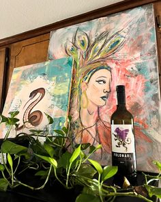 a bottle of wine sitting on top of a wooden shelf next to plants and paintings