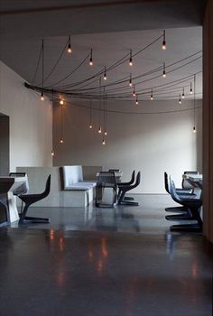 an empty room with many chairs and lights hanging from it's ceiling over the dining table