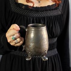 a woman in black dress holding a silver mug