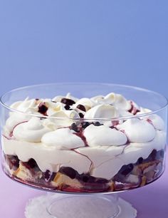 a cake with white frosting and blueberries in a glass dish on a purple surface