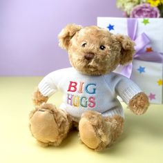 a teddy bear wearing a sweater sitting next to a gift box with flowers in the background