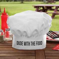 a white chef hat sitting on top of a wooden table next to utensils