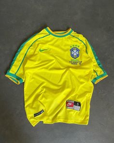 a yellow soccer jersey with green trim on the sleeves and chest, sitting on a gray floor