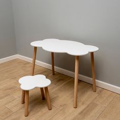 two white tables sitting on top of a hard wood floor next to a gray wall