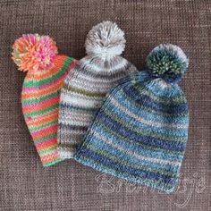 three knitted hats with pom poms on top of each other, one is multicolored