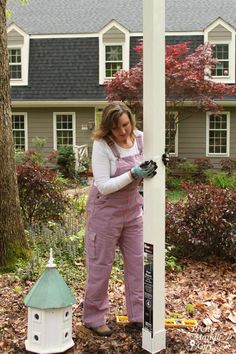 a woman in overalls and gloves is working on a pole with a birdhouse