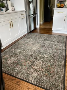 a large rug in the middle of a kitchen with white cabinets and wood flooring