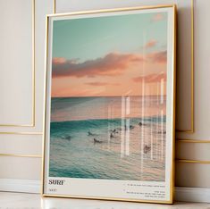 a framed photograph of surfers swimming in the ocean at sunset, with gold frame