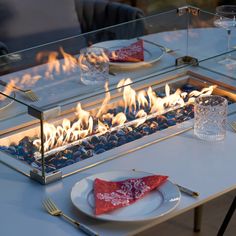 a table with a glass fire pit on top of it and place settings next to it