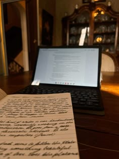 an open notebook sitting on top of a wooden desk next to a laptop computer,