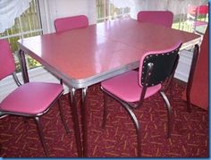 a pink table and four chairs in a room with red carpeted flooring, windows and curtains