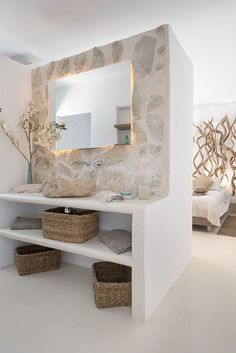 a white bathroom with stone walls and shelves on the wall is decorated with wicker baskets