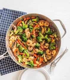 a pan filled with shrimp, broccoli and carrots on top of a table