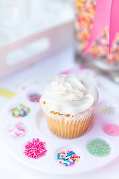 a cupcake with white frosting and sprinkles on a plate