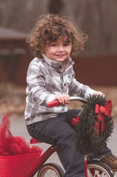 a young boy riding a red bicycle with a christmas wreath on the front basket and bow