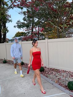 a woman in a red dress is walking next to a man