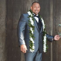 a man in a tuxedo and lei is standing next to a wooden wall