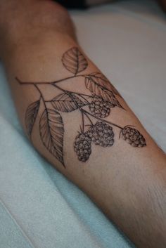 a person with a tattoo on their arm that has berries and leaves growing out of it