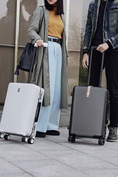 two people with suitcases standing on the side walk, one holding a handbag