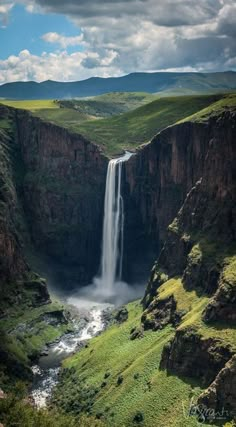 a large waterfall in the middle of a valley with green grass and mountains around it