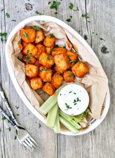 a white bowl filled with tater tots and celery on top of a wooden table