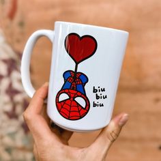 a person holding a coffee mug with a spiderman on it