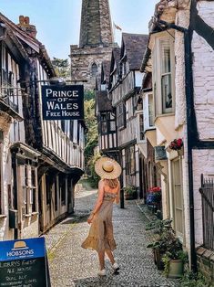 a woman walking down a cobblestone street in an old european village with tall buildings