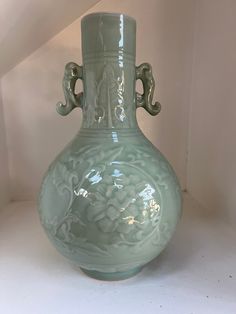 a light green vase sitting on top of a white table next to a stair case