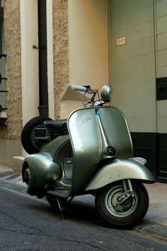 a green scooter parked on the side of a street next to a building