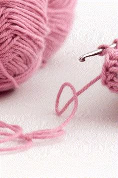 a pink ball of yarn with a crochet hook next to it on a white surface