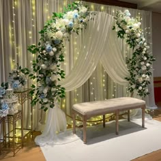 a white and blue wedding ceremony setup with flowers on the back wall, draped drapes and lights in the background