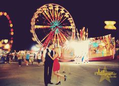 a man and woman standing next to each other in front of a ferris wheel at night