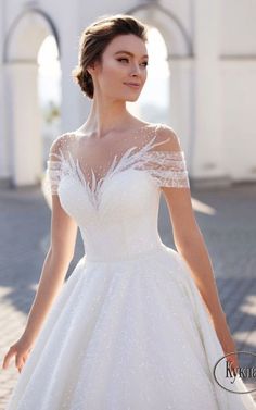 a woman in a white wedding dress standing on a brick walkway with her hands behind her back