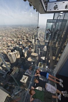 three people are standing on the glass floor of a high rise building looking at the city below