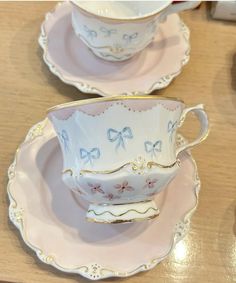 two tea cups and saucers with bows on them sitting on a wooden table top