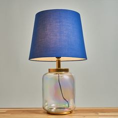 a glass lamp with a blue shade on it sitting on a wooden table next to a gray wall