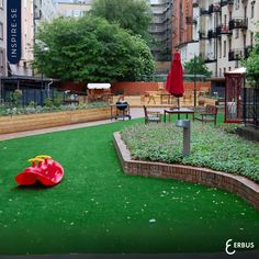 an outdoor play area with green grass and red slider in the foreground, surrounded by apartment buildings