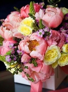 a bouquet of pink and yellow flowers in a white square vase on a black table